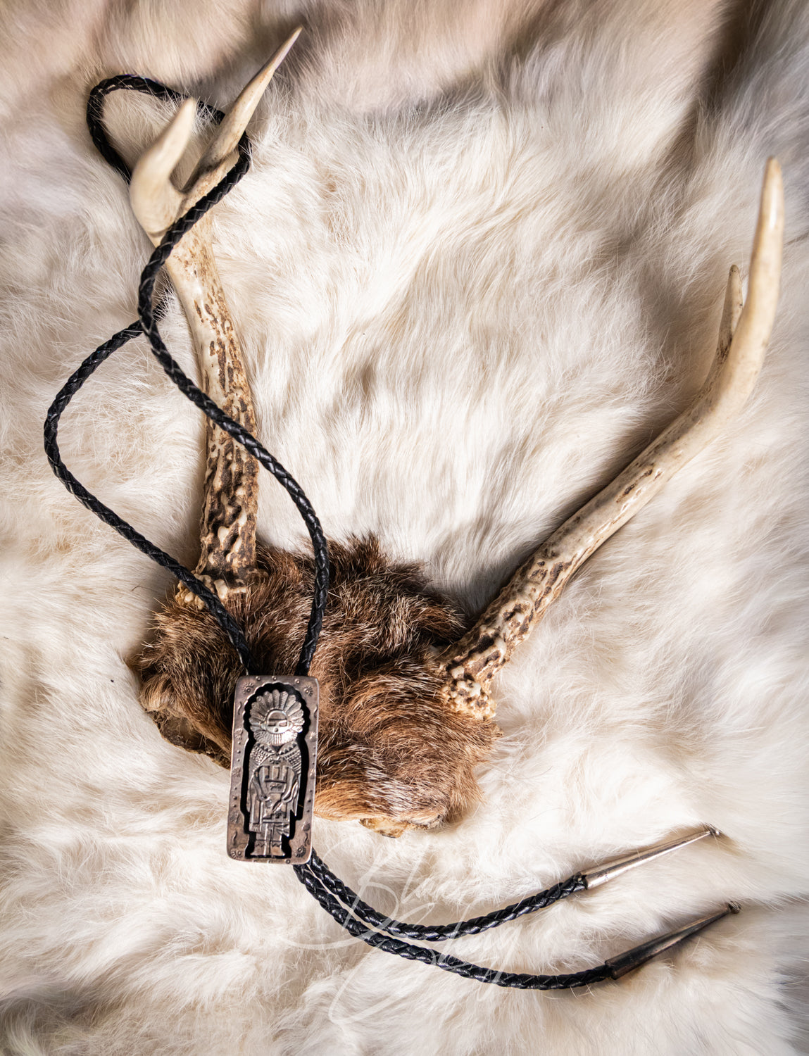 A rustic Native American style beaded necklace with a carved wooden pendant featuring an eagle design, threaded on a black cord with antler and fur elements, displayed on a white fur background.
