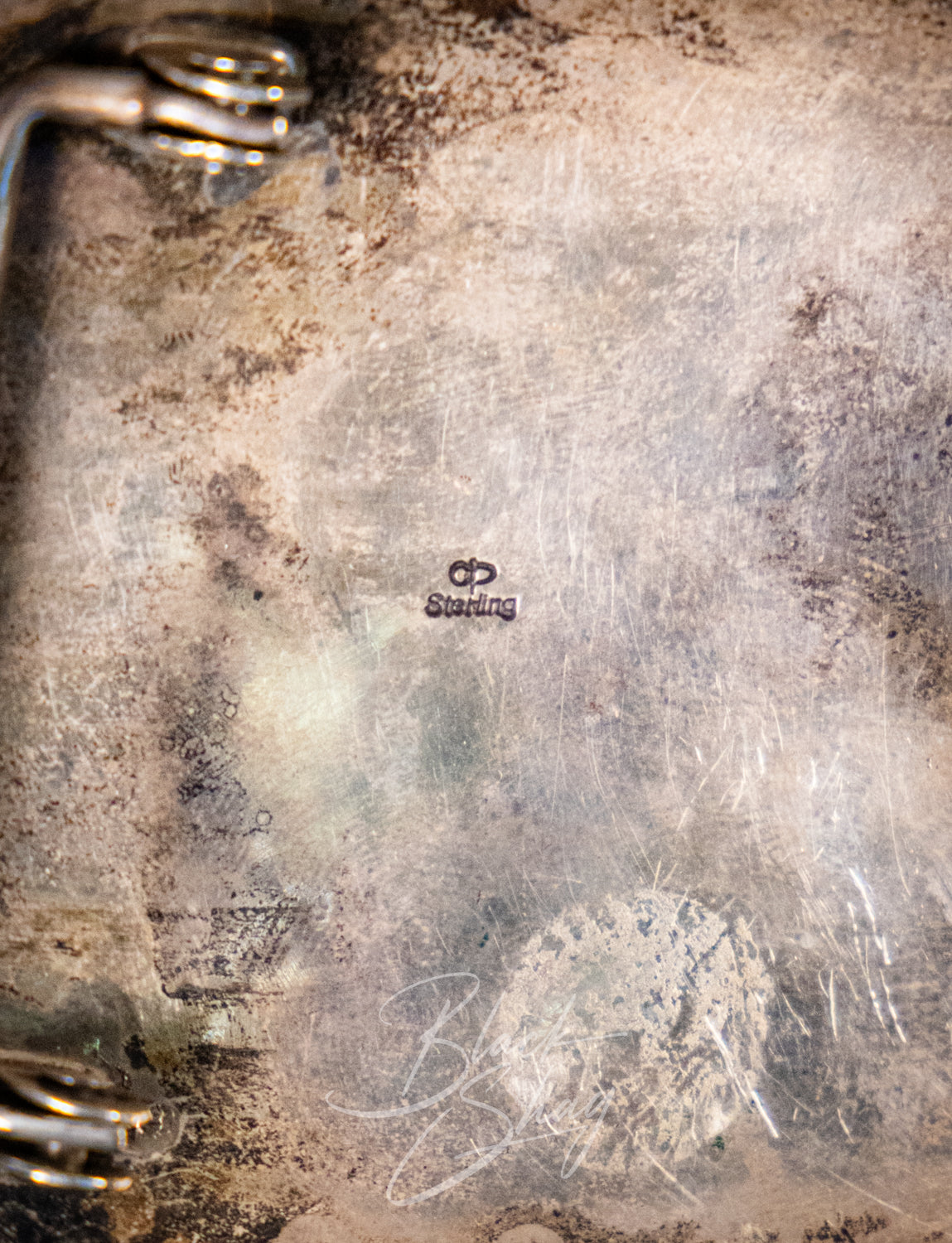 Close-up of the interior bottom surface of a tarnished silver tray or plate, showing a stamped 'Sutton' hallmark and heavy oxidation, scratches, and patina.